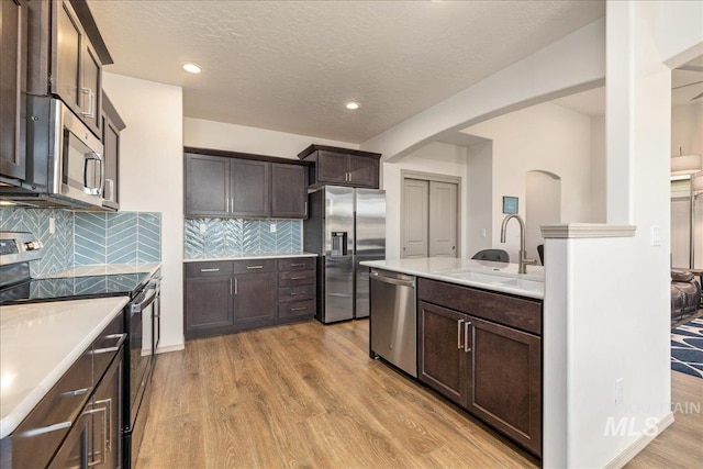 kitchen featuring light wood-style flooring, dark brown cabinets, appliances with stainless steel finishes, and a sink