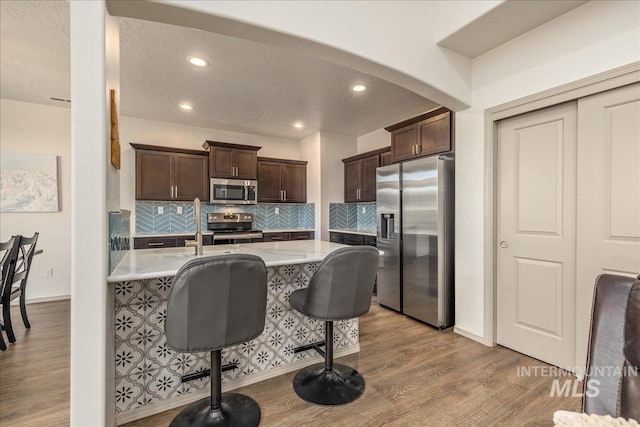 kitchen featuring backsplash, wood finished floors, stainless steel appliances, light countertops, and dark brown cabinets