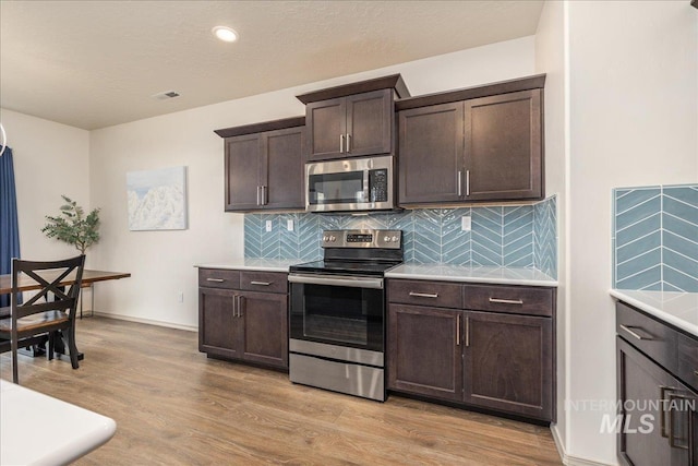 kitchen with backsplash, dark brown cabinetry, light countertops, light wood-style floors, and stainless steel appliances