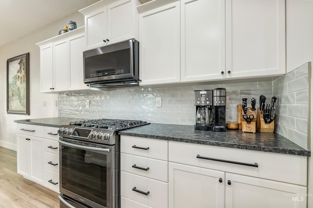2679 S Tristram Way, Meridian, ID 83642 - kitchen featuring appliances with stainless steel finishes, white cabinetry, light wood-type flooring, decorative backsplash, and dark stone countertops