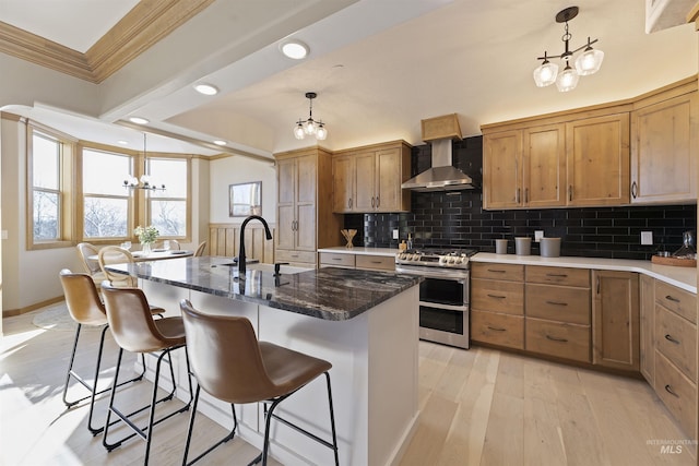 kitchen with an inviting chandelier, dark stone countertops, double oven range, a kitchen island with sink, and wall chimney range hood