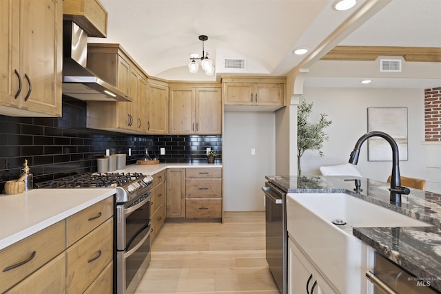 kitchen with lofted ceiling, hanging light fixtures, appliances with stainless steel finishes, light hardwood / wood-style floors, and wall chimney range hood