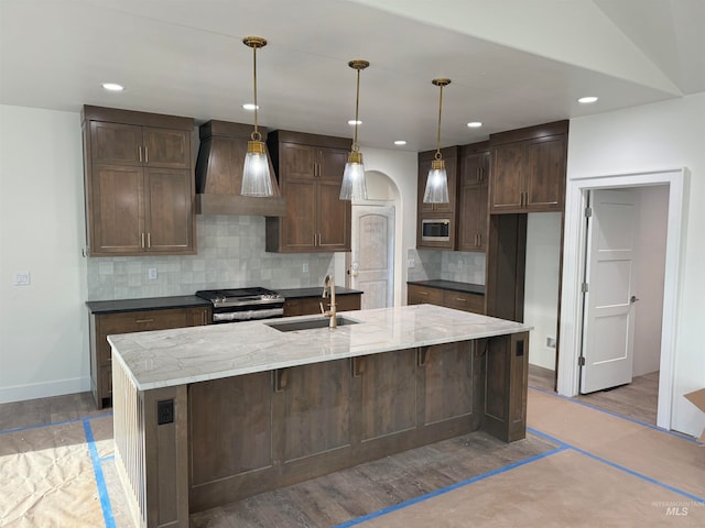 kitchen featuring sink, custom range hood, light stone countertops, pendant lighting, and appliances with stainless steel finishes