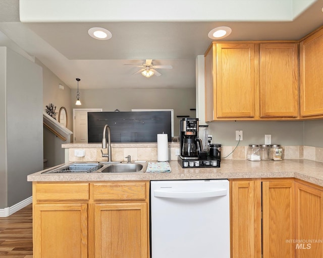 kitchen with wood finished floors, a peninsula, white dishwasher, ceiling fan, and a sink