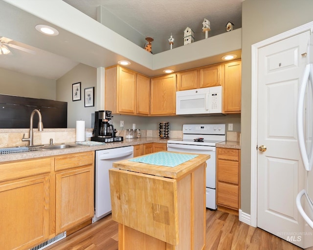 kitchen featuring white appliances, light brown cabinets, visible vents, a kitchen island, and a sink