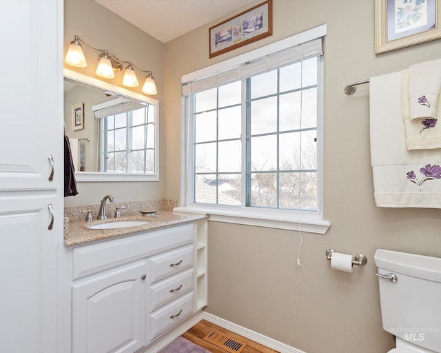 half bath with vanity, wood finished floors, toilet, and a healthy amount of sunlight