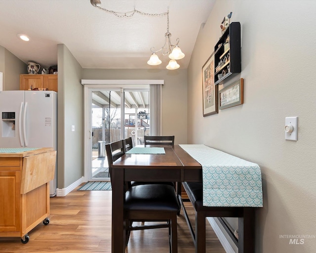 dining area with a notable chandelier, light wood-style flooring, lofted ceiling, and baseboards