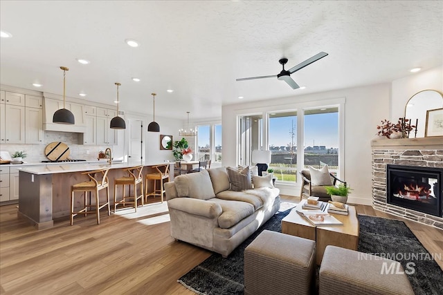 living room featuring a textured ceiling, ceiling fan, a fireplace, and light hardwood / wood-style flooring