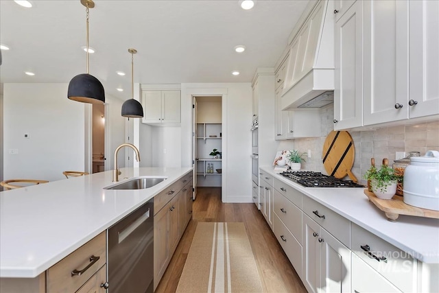 kitchen with sink, a large island with sink, white cabinets, custom range hood, and appliances with stainless steel finishes