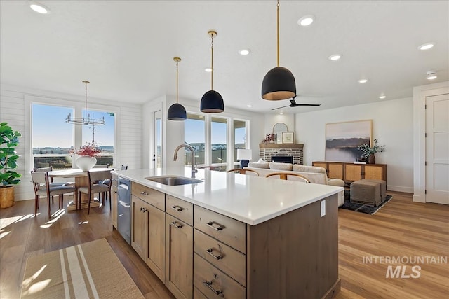 kitchen featuring sink, decorative light fixtures, a fireplace, ceiling fan with notable chandelier, and a center island with sink