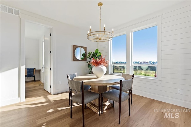 dining space with a notable chandelier, wood walls, and light wood-type flooring