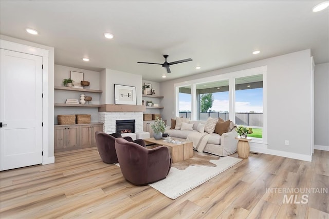 living room with a stone fireplace, ceiling fan, and light hardwood / wood-style flooring