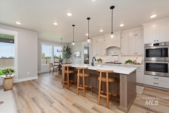 kitchen featuring hanging light fixtures, appliances with stainless steel finishes, an island with sink, light hardwood / wood-style floors, and white cabinets