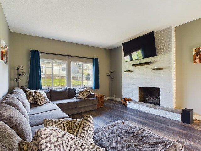 living room with dark hardwood / wood-style floors, brick wall, and a brick fireplace