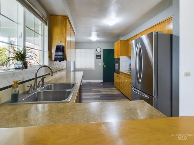 kitchen with dark hardwood / wood-style floors, decorative backsplash, sink, black oven, and stainless steel refrigerator