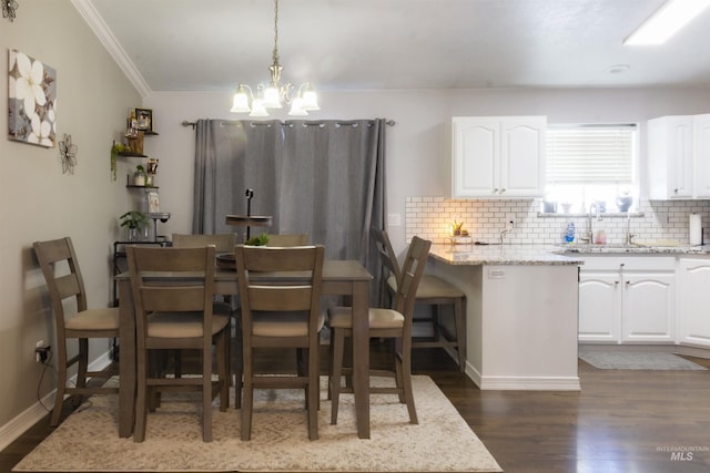 dining space with sink, a chandelier, crown molding, and dark wood-type flooring