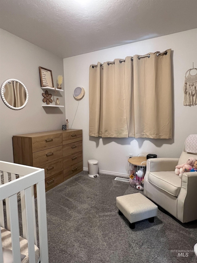 bedroom with dark colored carpet, a crib, and a textured ceiling