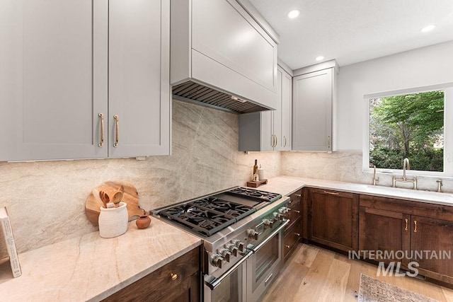 kitchen featuring a sink, range with two ovens, light wood finished floors, backsplash, and recessed lighting