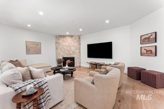 living room with light wood-type flooring, recessed lighting, and a stone fireplace