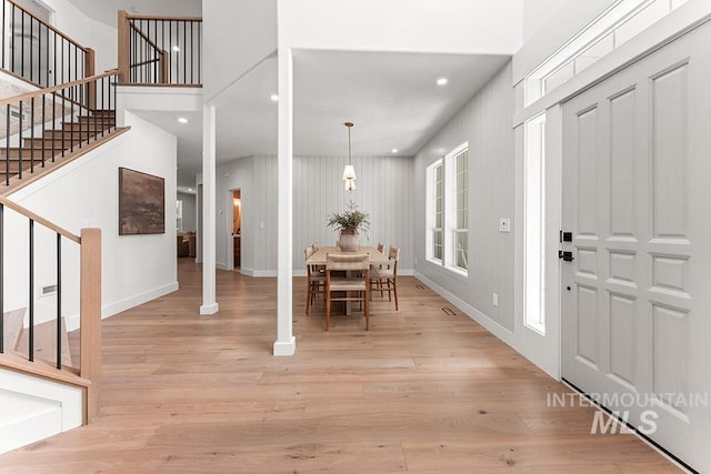 foyer entrance with stairway, light wood-style floors, recessed lighting, baseboards, and a towering ceiling