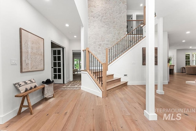 entrance foyer with light wood-type flooring, recessed lighting, stairs, baseboards, and a high ceiling
