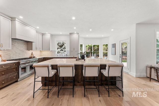kitchen with range with two ovens, a center island, light wood-type flooring, light countertops, and decorative backsplash