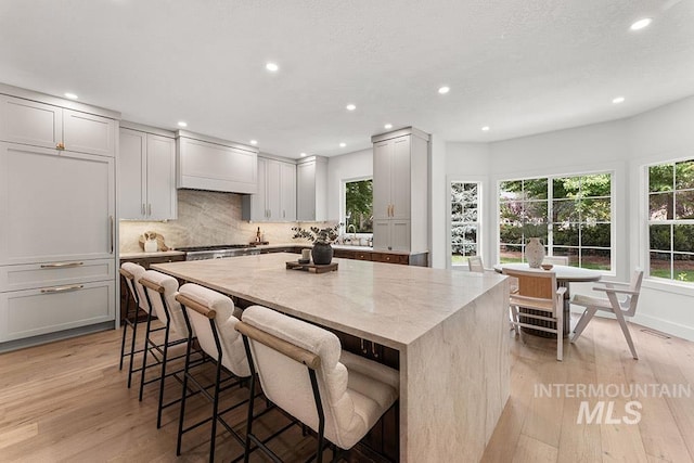 kitchen with light wood-type flooring, a kitchen island, recessed lighting, tasteful backsplash, and light stone counters