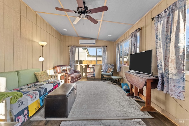 living room with lofted ceiling, ceiling fan, dark hardwood / wood-style floors, an AC wall unit, and wooden walls