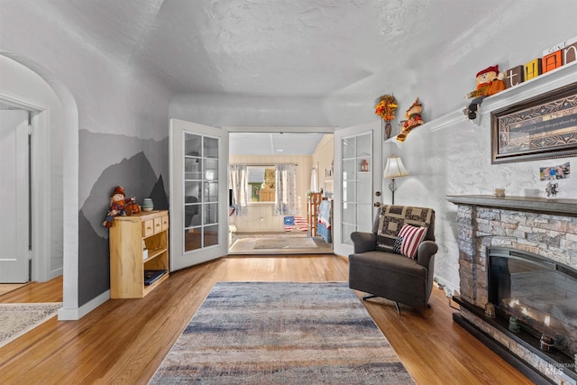 sitting room with a textured ceiling, a stone fireplace, wood-type flooring, and french doors