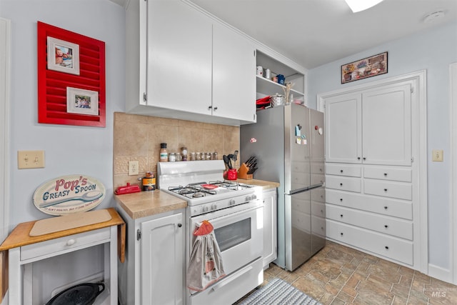 kitchen featuring backsplash, white range with gas cooktop, white cabinetry, and stainless steel refrigerator