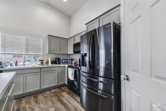 kitchen with lofted ceiling, sink, gray cabinetry, dark hardwood / wood-style floors, and black appliances