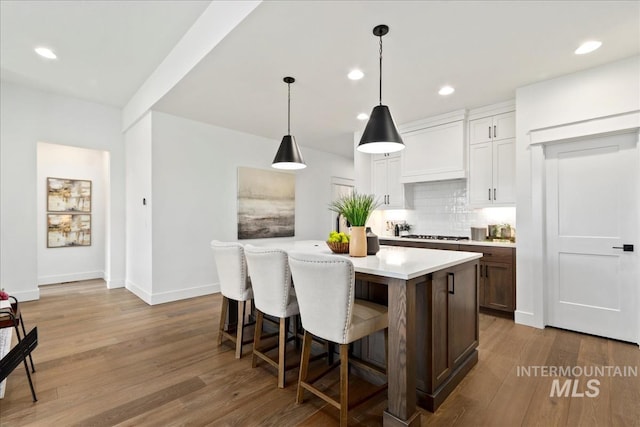 kitchen with dark wood-type flooring, light countertops, decorative backsplash, and custom exhaust hood