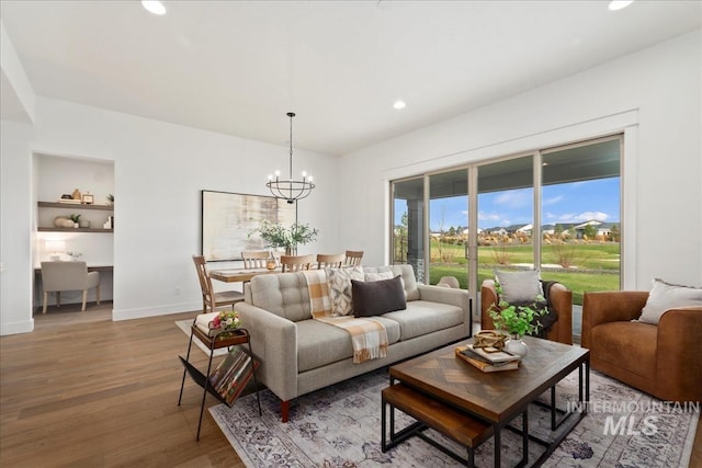 living room featuring baseboards, built in features, an inviting chandelier, light wood-type flooring, and recessed lighting