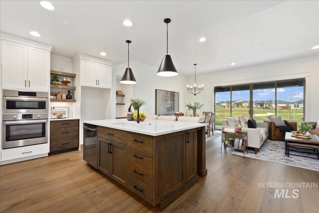 kitchen featuring decorative backsplash, dark brown cabinetry, a kitchen island with sink, pendant lighting, and light hardwood / wood-style floors