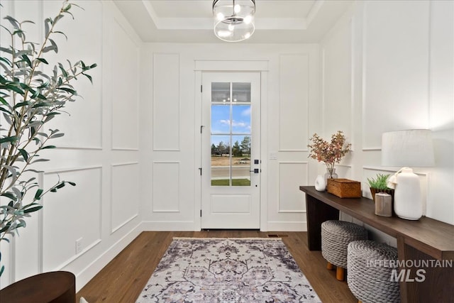 entryway featuring dark wood-style floors, a tray ceiling, and a decorative wall