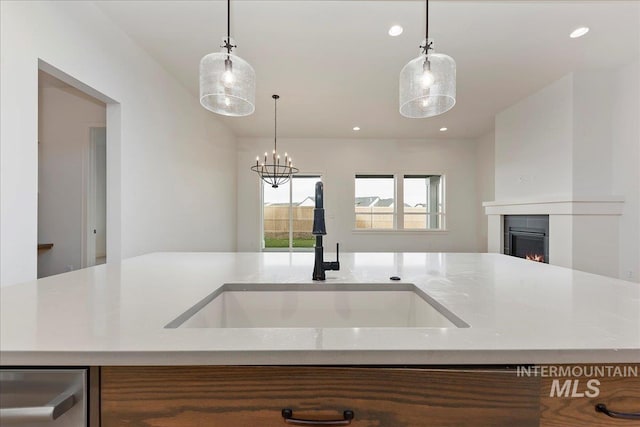 kitchen featuring pendant lighting, an inviting chandelier, a kitchen island with sink, and sink