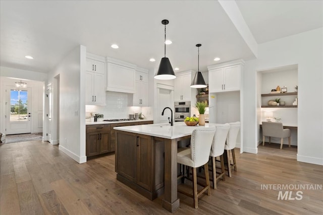 kitchen with stainless steel appliances, light countertops, a sink, an island with sink, and wood finished floors