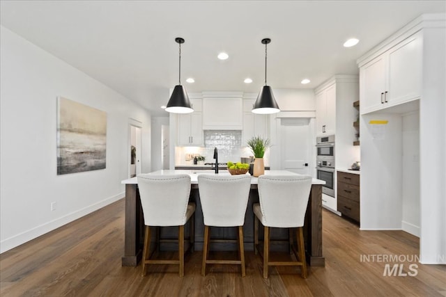 kitchen featuring white cabinets, dark wood-type flooring, a kitchen island with sink, light countertops, and backsplash