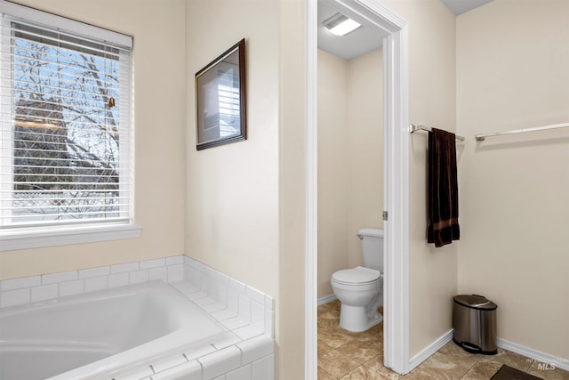 bathroom with a wealth of natural light, tiled bath, and toilet