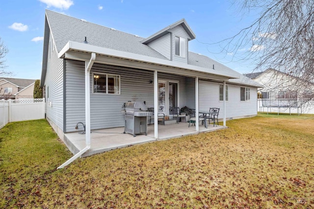 rear view of property featuring a trampoline, a patio, and a lawn