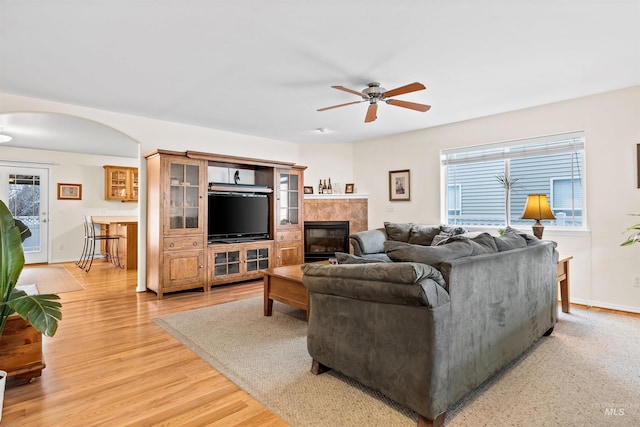 living room featuring a tile fireplace, ceiling fan, and light wood-type flooring