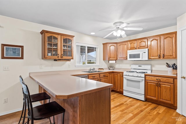 kitchen featuring sink, white appliances, light hardwood / wood-style flooring, kitchen peninsula, and a breakfast bar area