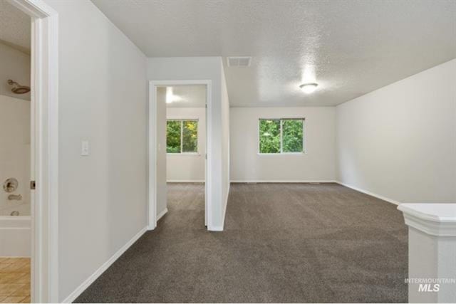 carpeted empty room featuring visible vents, a textured ceiling, and baseboards