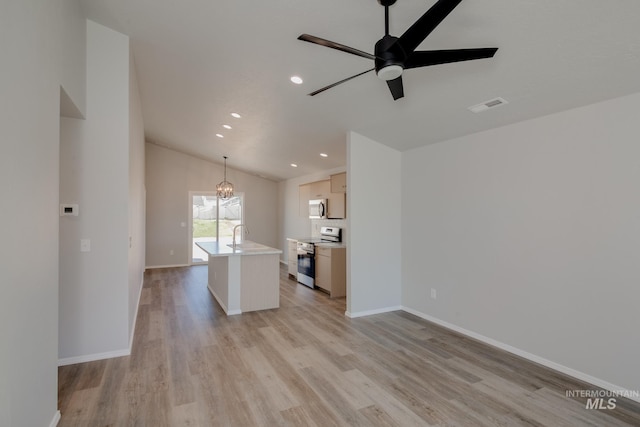 kitchen featuring lofted ceiling, light hardwood / wood-style flooring, appliances with stainless steel finishes, hanging light fixtures, and an island with sink