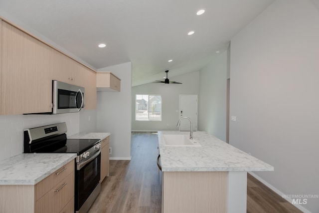 kitchen with sink, vaulted ceiling, light brown cabinets, appliances with stainless steel finishes, and an island with sink