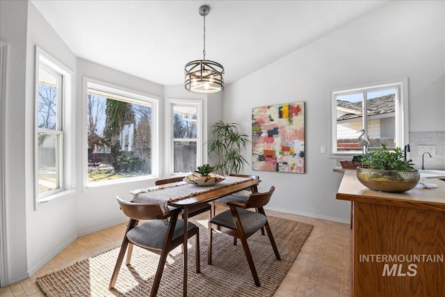 dining area with a chandelier, lofted ceiling, plenty of natural light, and baseboards