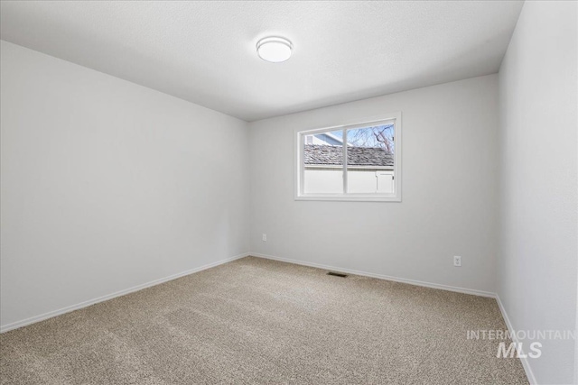 carpeted spare room featuring visible vents, a textured ceiling, and baseboards