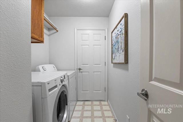 washroom featuring a textured wall, light floors, washer and clothes dryer, and cabinet space