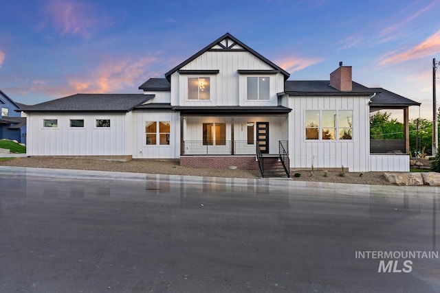 back of property at dusk featuring board and batten siding, covered porch, a chimney, and a shingled roof