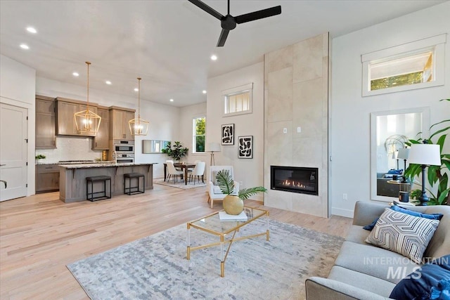 living area featuring recessed lighting, ceiling fan, light wood-type flooring, and a tiled fireplace
